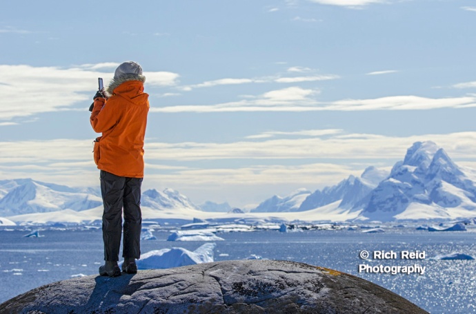 A person enjoying the view and Luigi Peak from Booth Island at Port Charcot in Antarctica.